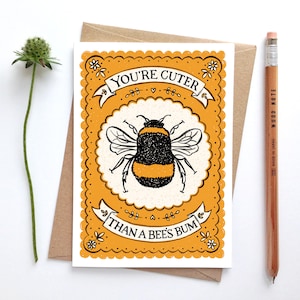 May include: A yellow and white card with a black and yellow bumblebee illustration. The card has a scalloped border and the text "You're cuter than a bee's bum".