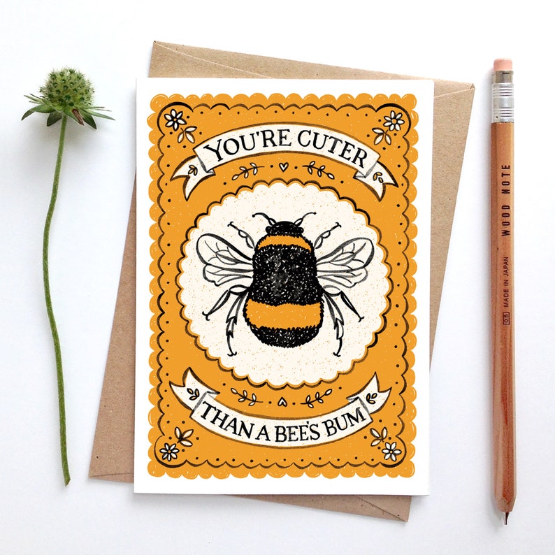 May include: A yellow and white card with a black and yellow bumblebee illustration. The card has a scalloped border and the text "You're cuter than a bee's bum".