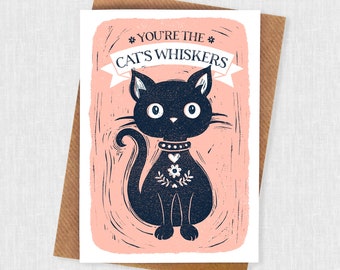 May include: A pink greeting card with a black cat illustration. The card says "You're the Cat's Whiskers" with a banner above the cat.