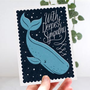 May include: A sympathy card with a blue whale illustration on a dark blue background with white stars. The card reads "With Deepest Sympathy" in white script. The card has a scalloped border.