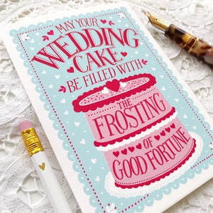 May include: A light blue card with a pink and white wedding cake illustration. The card reads "May your wedding cake be filled with the frosting of good fortune".