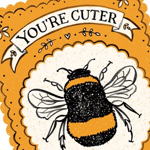 May include: A yellow and black bumblebee with wings outstretched, surrounded by a white circle with a scalloped edge. The circle is on a yellow background with a banner that reads "YOU'RE CUTER".