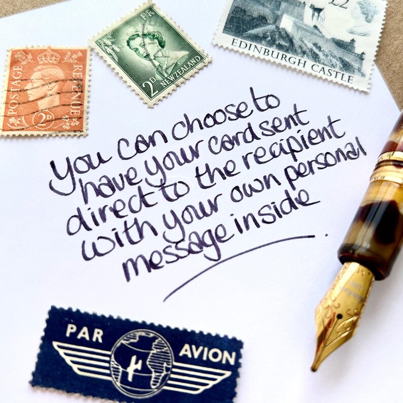 May include: A white paper with handwritten text and vintage stamps. The text says, "You can choose to have your card sent direct to the recipient with your own personal message inside." A fountain pen is visible. Stamps are also present.
