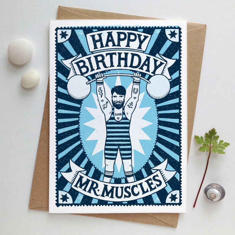 Pu&ograve; includere: Un biglietto di auguri di compleanno blu e bianco con un'illustrazione di un uomo che solleva pesi. Il biglietto dice "Buon compleanno Mr. Muscles".