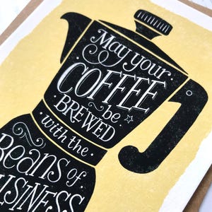 May include: A yellow card with a black illustration of a coffee pot. The text reads "May your coffee be brewed with the beans of business."