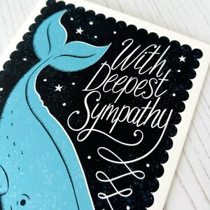 May include: A sympathy card with a light blue whale design on a black backdrop with white stars. The card displays the words "With Deepest Sympathy" in white script, set within a scalloped border.