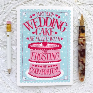 May include: A light blue card with a white scalloped border. The card features a pink and red wedding cake with the text "May your wedding cake be filled with the frosting of good fortune".
