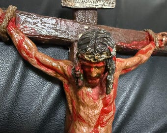 May include: A wooden crucifix with a depiction of Jesus Christ. The figure is painted in a realistic style with red paint representing blood. The inscription on the cross reads "INRI".