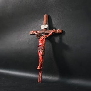 Könnte beinhalten: Ein Holzkruzifix mit einer roten und weißen Figur von Jesus Christus. Die Figur ist mit Blut dargestellt, das aus ihren Wunden tropft.