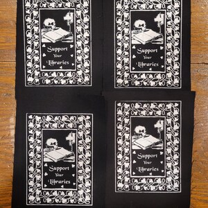 Puede incluir: Cuatro parches negros con un dise&ntilde;o blanco que presenta una calavera, libros y una l&aacute;mpara. El texto "Support Your Libraries" se muestra en una fuente decorativa. Los parches son rectangulares y probablemente para coser o planchar sobre tela.