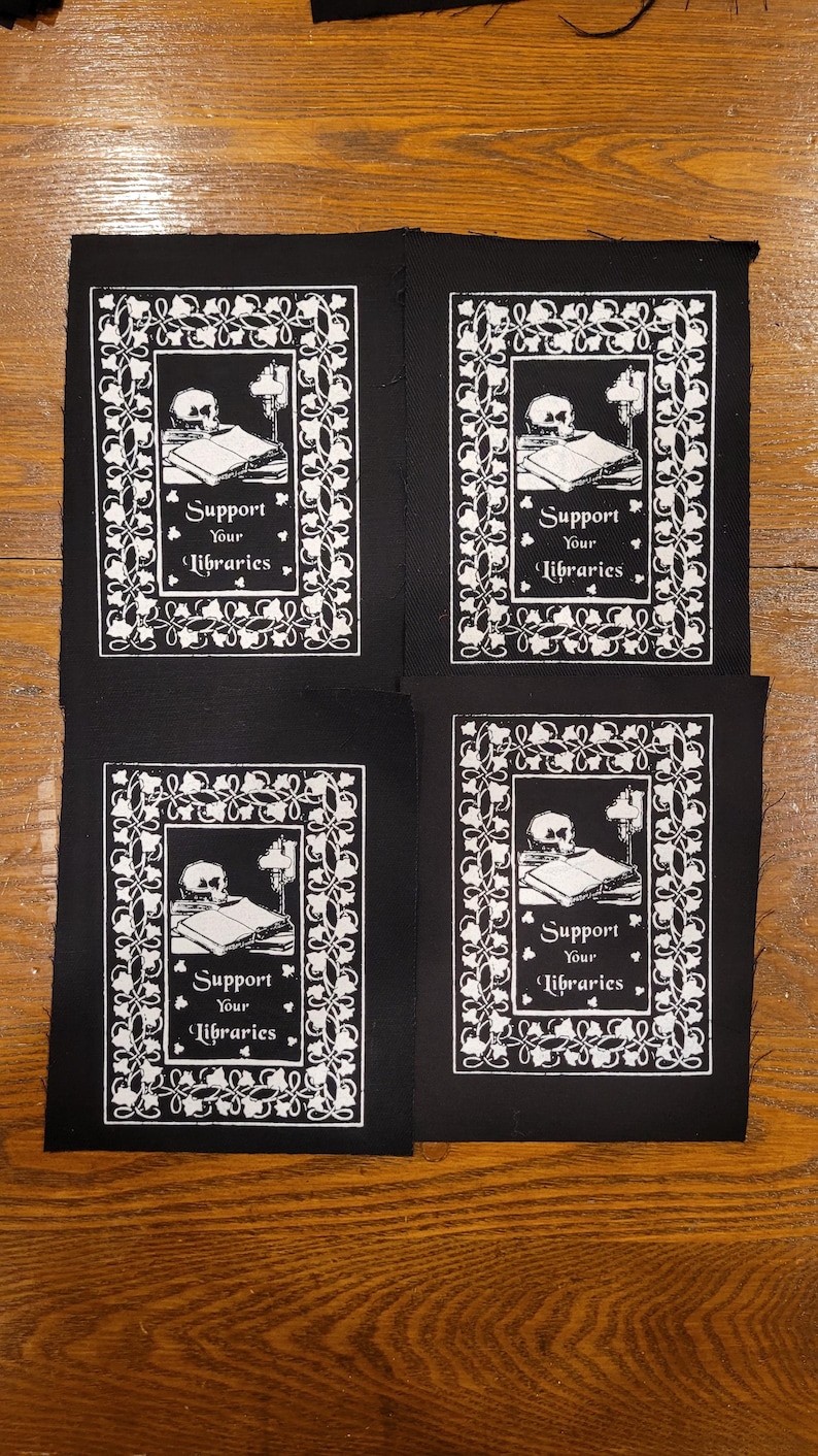 Puede incluir: Cuatro parches negros con un dise&ntilde;o blanco que presenta una calavera, libros y una l&aacute;mpara. El texto "Support Your Libraries" se muestra en una fuente decorativa. Los parches son rectangulares y probablemente para coser o planchar sobre tela.