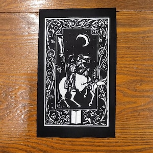 Op de afbeelding: Zwart-witte patch met een ridder te paard onder een halve maan. Het ontwerp bevat sierlijke randdetails en een gestileerde illustratie van een middeleeuwse scène. De patch is rechthoekig.