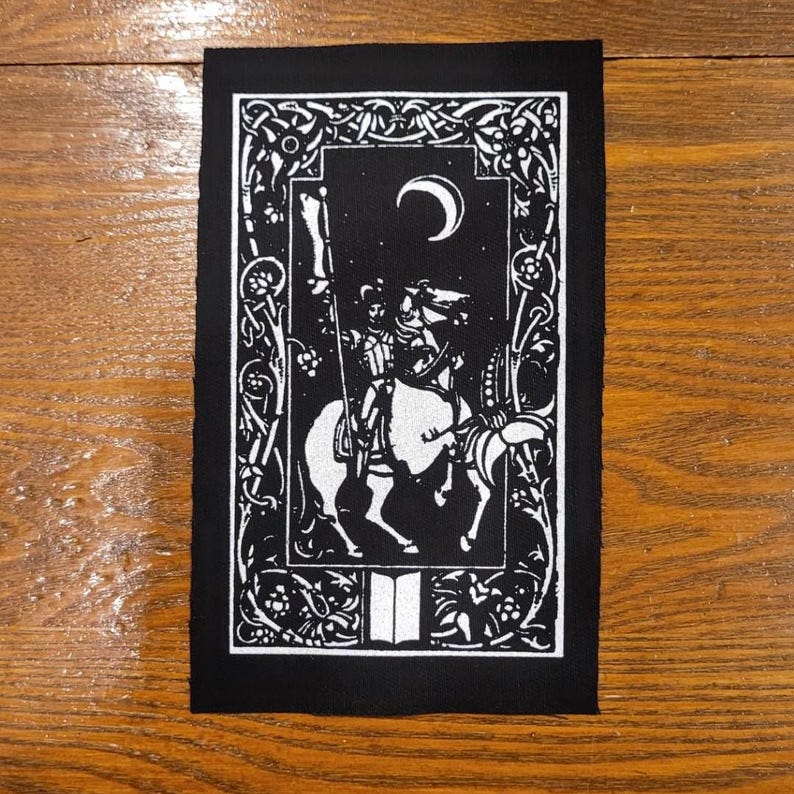 May include: Black and white patch depicting a knight on horseback beneath a crescent moon. The design includes an ornate border and a stylized illustration of a medieval scene. The patch is rectangular in shape.