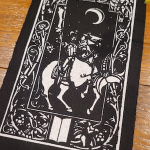 May include: Black and white patch depicting a knight on horseback beneath a crescent moon. The design includes floral and scrollwork borders. The knight is in full armour, and the horse is detailed.