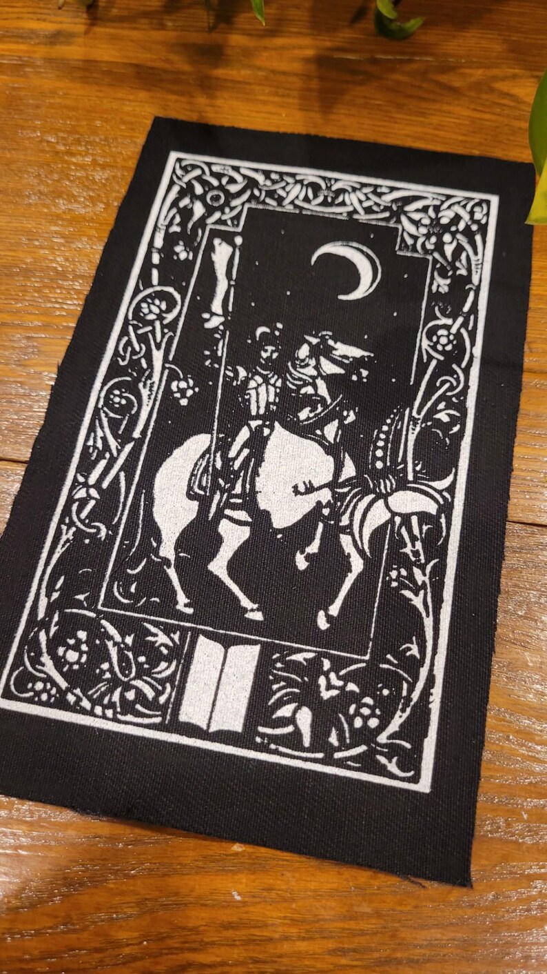 May include: Black and white patch depicting a knight on horseback beneath a crescent moon. The design includes floral and scrollwork borders. The knight is in full armour, and the horse is detailed.