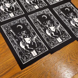 May include: A collection of black and white tarot card patches, each depicting a knight on horseback beneath a crescent moon. The patches have decorative borders and are laid out on a wooden surface. The design is repeated.