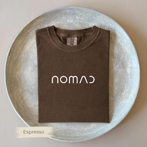 A brown t-shirt with the word "NOMAD" printed on it, laid out on a white plate.