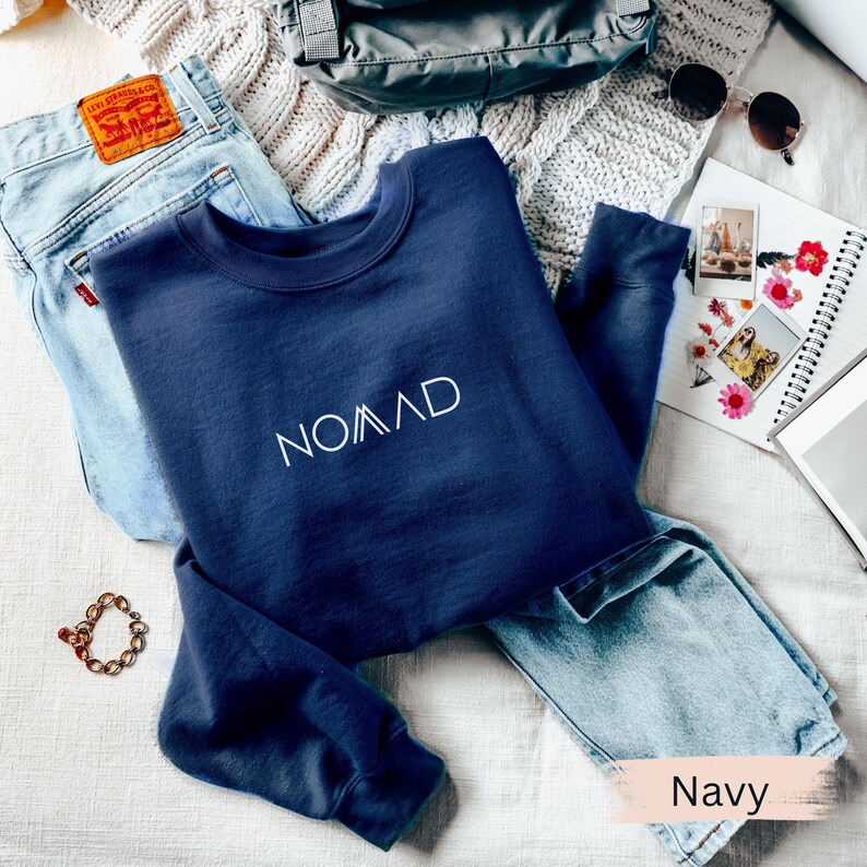 A navy blue sweatshirt with the word "NOMAD" printed on it, along with a pair of jeans and other clothing items, are laid out on a surface.