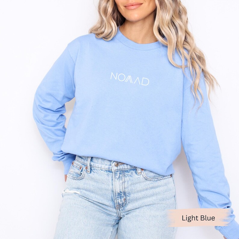 A woman wearing a light blue long-sleeved shirt with the word "Noah" printed on it, paired with light blue jeans.
