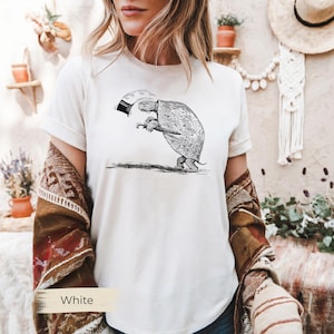 May include: White t-shirt featuring a black and white illustration of a turtle holding an umbrella. The turtle is drawn in a detailed, vintage style. The word "White" is printed at the bottom of the shirt.