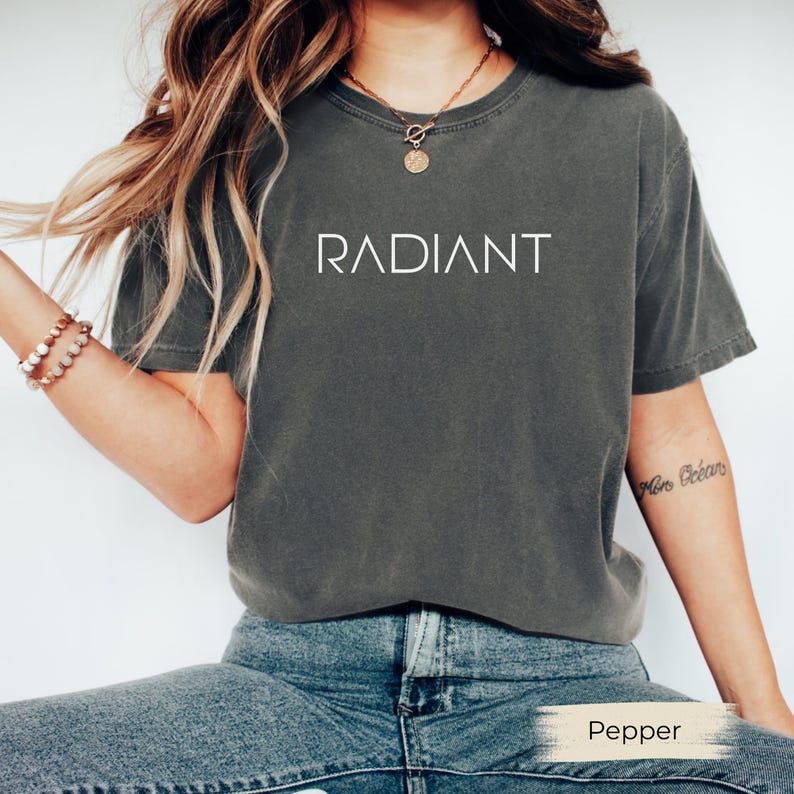 A woman wearing a gray t-shirt with the word "RADIANT" printed on it, paired with blue jeans and bracelets.
