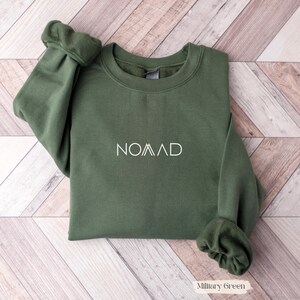 A green sweatshirt with the word "NOMAD" printed on it, laid out on a wooden surface.