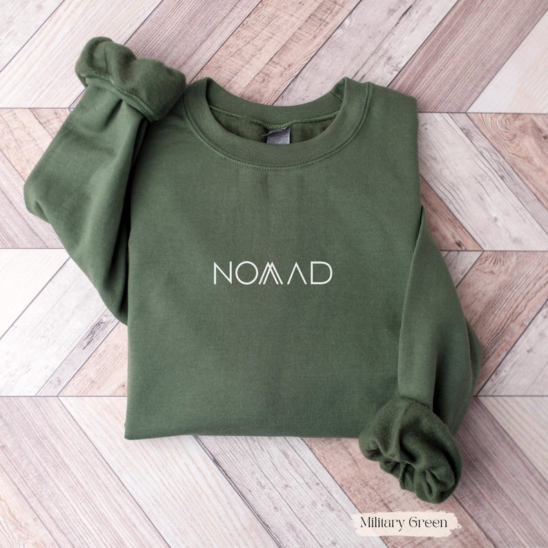 A green sweatshirt with the word "NOMAD" printed on it, laid out on a wooden surface.