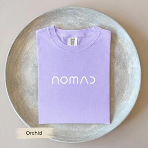 A purple t-shirt with the word "Orchid" printed on it, laid out on a gray plate.