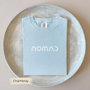 A light blue t-shirt with the word "NOMAD" printed on it, laid out on a round, gray plate.