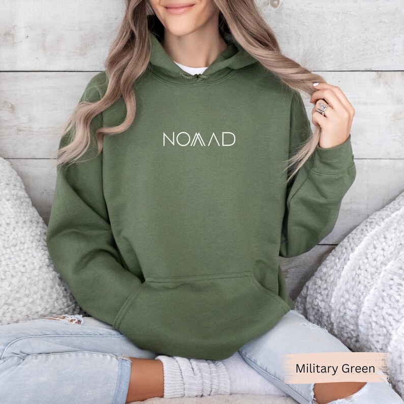 A woman wearing a green hoodie with the word "NOMAD" printed on it, sitting on a couch with her hair in a ponytail.
