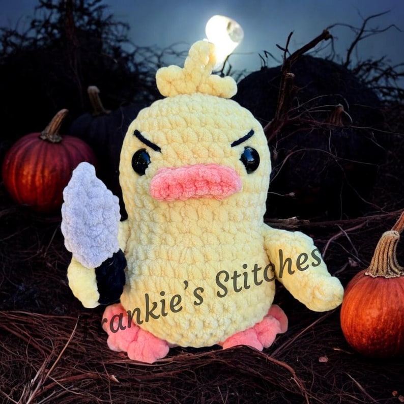 Puede incluir: Un pato de ganchillo amarillo hecho a mano con ojos negros, un pico rosa y pies rosas, sosteniendo un cuchillo gris y negro. El pato tiene una expresi&oacute;n de enfado. El texto "Frankie's Stitches" est&aacute; en el pato. Las calabazas est&aacute;n en el fondo.