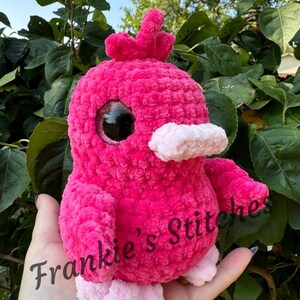 Puede incluir: Un p&aacute;jaro rosa de peluche hecho a mano, con grandes ojos negros, un pico rosa claro y patas a juego. El p&aacute;jaro tiene un aspecto texturizado y difuso y una peque&ntilde;a cresta. El texto "Frankie's Stitches" es visible en el p&aacute;jaro.