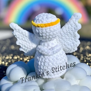 Può includere: Un angelo bianco all'uncinetto con un alone giallo e grandi ali. L'angelo è in piedi su oggetti bianchi a forma di nuvola. Il testo "Frankie's Stitches" è scritto in corsivo sulle nuvole. Un arcobaleno è visibile sullo sfondo.