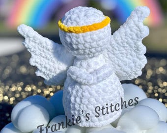 May include: A white crochet angel with a yellow halo and large wings. The angel is standing on white cloud-shaped objects. The text "Frankie's Stitches" is written in cursive on the clouds. A rainbow is visible in the background.