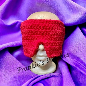 May include: A red crocheted sleep mask with a textured surface. The mask is on a mannequin head.