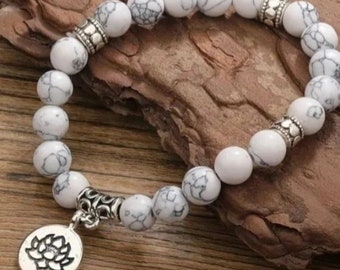 May include: White beaded bracelet with a silver lotus flower charm. The bracelet is made of white beads with black marbling and silver spacers.