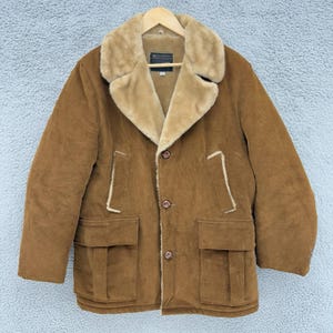 May include: A brown corduroy jacket with a tan faux fur collar and lining. The jacket features two front pockets, a button closure, and a label on the collar. It is displayed on a wooden hanger.