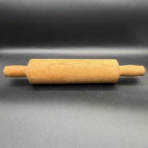 May include: A light brown wooden rolling pin. The rolling pin has a cylindrical body and two handles. This kitchen tool is designed for rolling out dough. The rolling pin measures approximately 30 cm in length.
