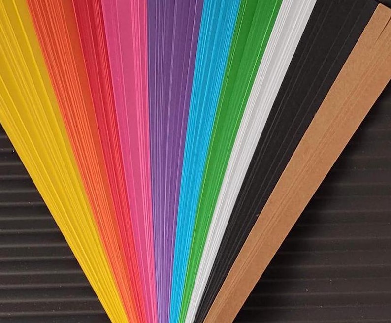 10 Colors Quilling Paper Strips - High Quality 180 gsm Rainbow Palette Set DIY Kit, Typography & 3D Effect, Perfect Craft Supplies. Quilling paper strips in various widths, including 3mm, 5mm, 7mm, and 10mm. The paper is 180 GSM and comes in a pack of 100 strips. Best for - On-edge quilling, Lettering, Outline quilling and Structured designs'.The colors are black, brown, white, green, blue, purple, pink, red, orange, and yellow. The strips are arranged in a vertical row.
