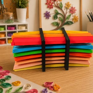 Peut inclure: Une pile multicolore de longues bandes de papier fines, organisées par couleur dans un support en plastique noir. Les bandes sont disposées en couches horizontales aux tons jaune, orange, rouge, bleu, vert et rose clair, maintenues par deux supports noirs.
