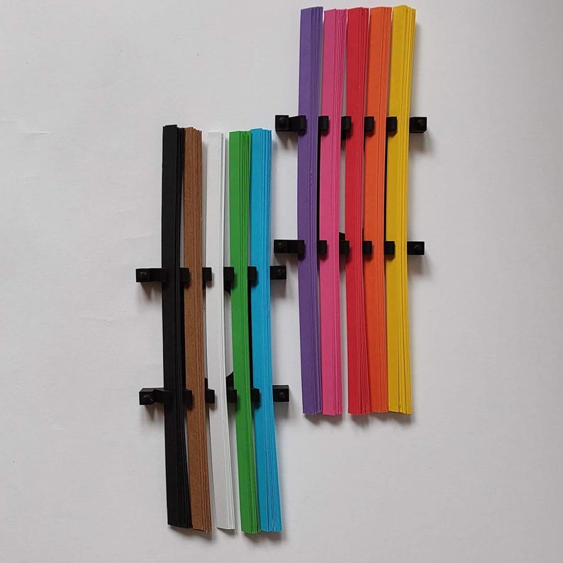 10 Colors Quilling Paper Strips - High Quality 180 gsm Rainbow Palette Set DIY Kit, Typography & 3D Effect, Perfect Craft Supplies. Quilling paper strips in various widths, including 3mm, 5mm, 7mm, and 10mm. The paper is 180 GSM and comes in a pack of 100 strips. Best for - On-edge quilling, Lettering, Outline quilling and Structured designs'.The colors are black, brown, white, green, blue, purple, pink, red, orange, and yellow. The strips are arranged in a vertical row.
