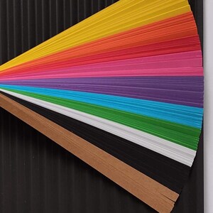 10 Colors Quilling Paper Strips - High Quality 180 gsm Rainbow Palette Set DIY Kit, Typography & 3D Effect, Perfect Craft Supplies. Quilling paper strips in various widths, including 3mm, 5mm, 7mm, and 10mm. The paper is 180 GSM and comes in a pack of 100 strips. Best for - On-edge quilling, Lettering, Outline quilling and Structured designs'.The colors are black, brown, white, green, blue, purple, pink, red, orange, and yellow. The strips are arranged in a vertical row.