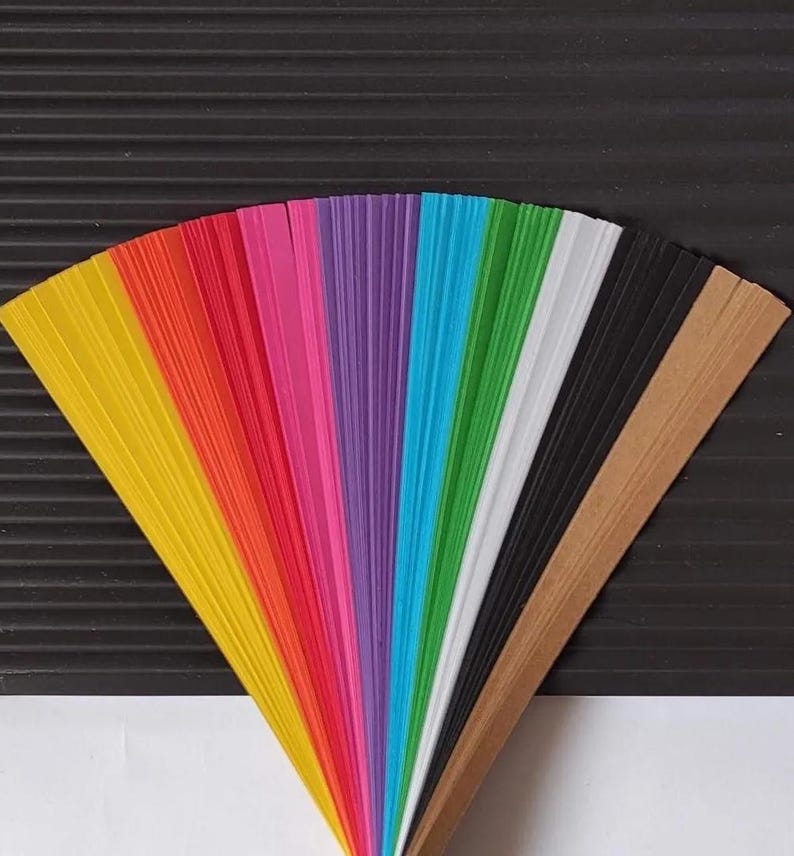 10 Colors Quilling Paper Strips - High Quality 180 gsm Rainbow Palette Set DIY Kit, Typography & 3D Effect, Perfect Craft Supplies. Quilling paper strips in various widths, including 3mm, 5mm, 7mm, and 10mm. The paper is 180 GSM and comes in a pack of 100 strips. Best for - On-edge quilling, Lettering, Outline quilling and Structured designs'.The colors are black, brown, white, green, blue, purple, pink, red, orange, and yellow. The strips are arranged in a vertical row.