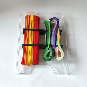 May include: A clear plastic container with two compartments holds colorful paper strips. One compartment has red, orange, and yellow strips. The other compartment has green, purple, and light blue strips.
