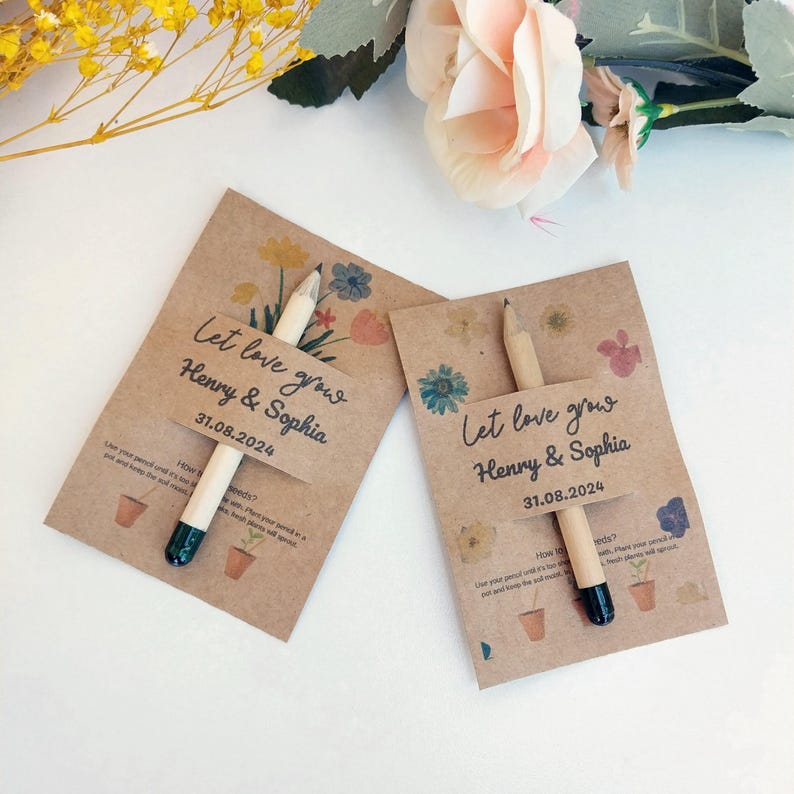 Op de afbeelding: Twee huwelijksbedankjes van kraftpapier met potloden. Elke kaart leest "Let love grow Henry & Sophia 31.08.2024" met bloemenillustraties. De potloden hebben een natuurlijke houten afwerking en een donkergroene punt.