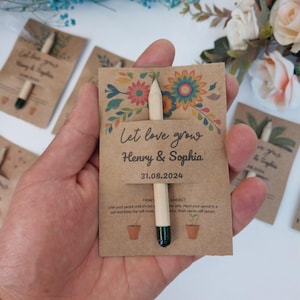 Op de afbeelding: Een zaadverpakking van kraftpapier met een potlood. De verpakking is versierd met bloemmotieven en de tekst "Let love grow Henry & Sophia 31.08.2024". Het potlood heeft een groene punt en zit in de verpakking.
