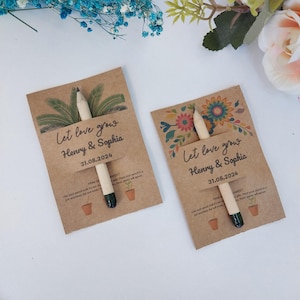 Op de afbeelding: Twee bruiloftbedankjes van kraftpapier met potloden. Elke kaart leest "Let love grow" met de namen "Henry & Sophia" en de datum "31.08.2024". E&eacute;n kaart heeft een palmboomontwerp, de andere een bloemenontwerp.