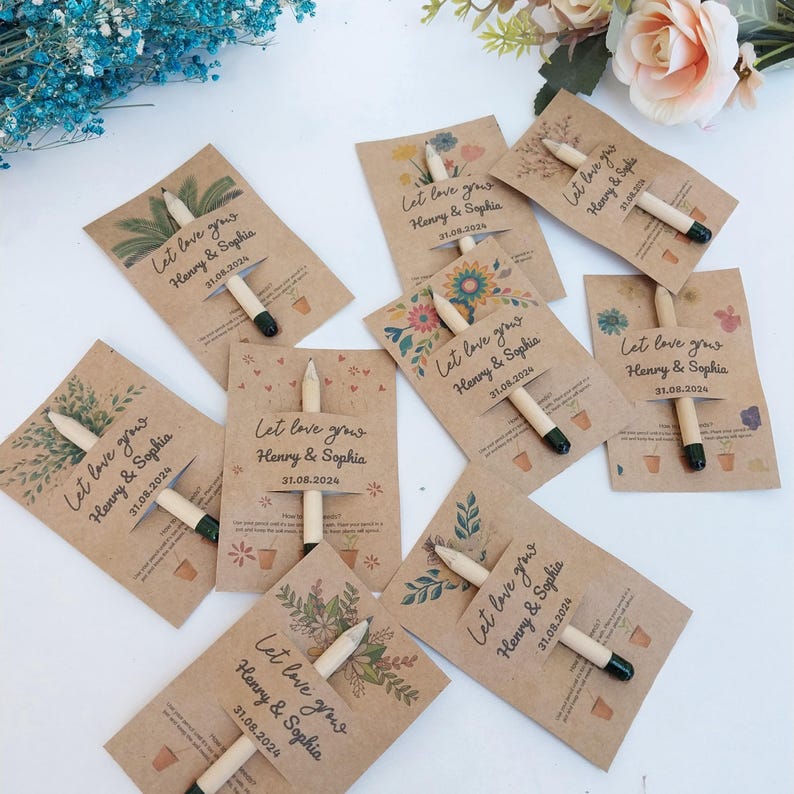 Op de afbeelding: Een verzameling kraftpapieren zaadzakjes met potloden eraan bevestigd. Elk zakje is versierd met bloemen- of botanische ontwerpen en de tekst "Let love grow Henry & Sophia 31.08.2024". De potloden hebben een natuurlijke houten afwerking met een zwarte punt.