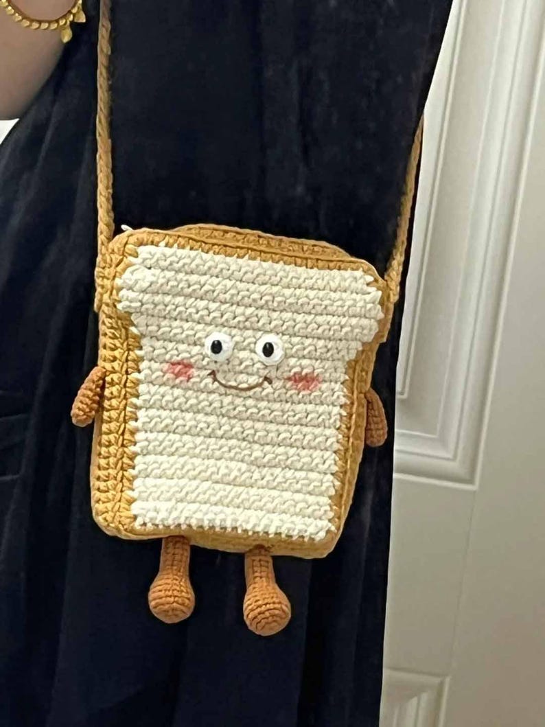 K&ouml;nnte beinhalten: Eine geh&auml;kelte braune und wei&szlig;e Tasche in Form eines Brotes mit einem l&auml;chelnden Gesicht und zwei kleinen Beinen.