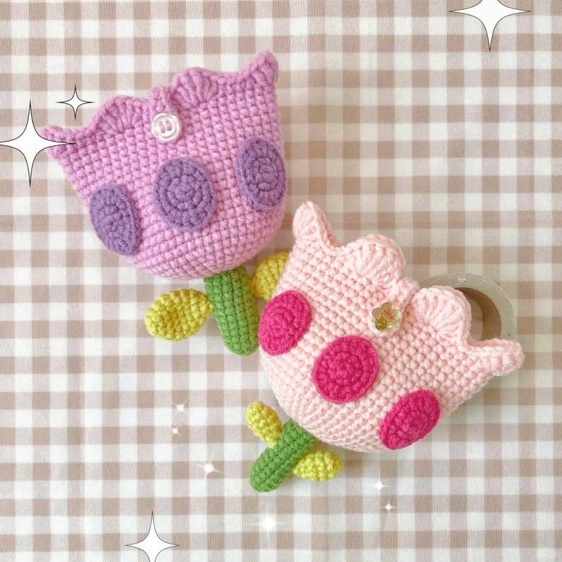 May include: Two crocheted tulip-shaped flower decorations. One is pink with pink polka dots and the other is purple with purple polka dots. Both have green stems and leaves.